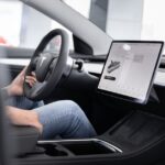 Interior of an electric car showing steering wheel and large touchscreen display, indicating modern technology.