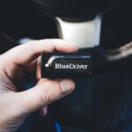 Close-up of a hand holding a BlueDriver wireless diagnostic tool inside a vehicle.