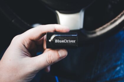 Close-up of a hand holding a BlueDriver wireless diagnostic tool inside a vehicle.