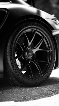 Black and white close-up of a sleek sports car wheel, showcasing its detailed design.