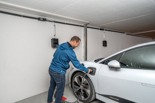 A man connects an electric car to a charging station in a modern indoor garage setting.