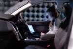 Woman working on a laptop inside a car, testing sound engineering in an isolated chamber.