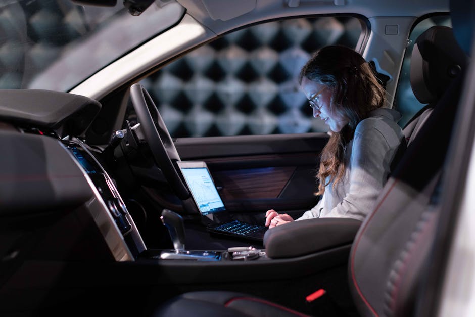 Woman working on a laptop inside a car, testing sound engineering in an isolated chamber.