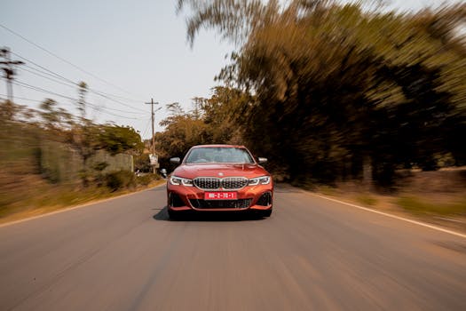 Front view of a shiny red luxury car speeding on a tree-lined road in Mumbai.