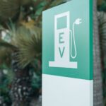 Close-up of a green and white electric vehicle charging station sign with nature background.
