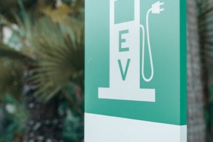 Close-up of a green and white electric vehicle charging station sign with nature background.